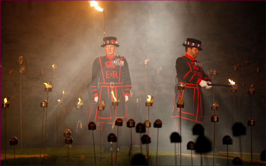 Two Beefeaters, one lighting the torches one keeping an eye on proceedings